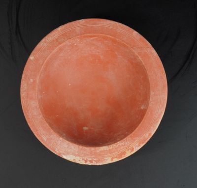 un bol orange posé sur une table noire, près d'un mur noir