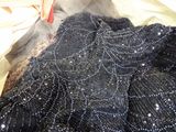 a black dress with silver beads on it laying on a bed