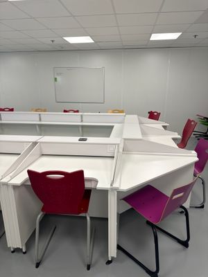 des tables et des chaises dans une salle de classe avec un tableau blanc accroché au mur