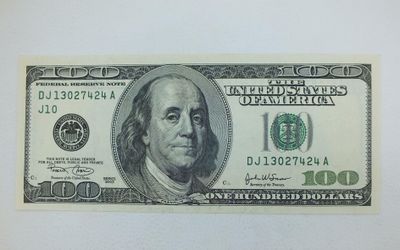 un billet de cent dollars posé sur une surface blanche