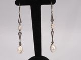 a pair of pearl and silver earrings on a black stand