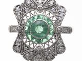a close up of a ring with a green stone surrounded by diamonds