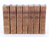 six old books lined up in a row on a white surface