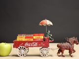 a toy horse pulling a cart with coca cola on it next to an apple