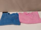 two pink and blue sweaters sitting on top of a white table