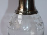 un vase en verre muni d'un couvercle en argent, posé sur une surface blanche
