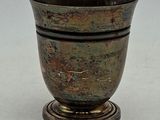 une tasse en métal posée sur un socle en bois, sur une surface blanche