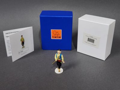 La figurine est assise à côté d'une boîte sur laquelle est posée une carte.