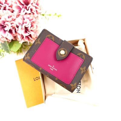 a pink and brown wallet sitting on a box next to a pink flower