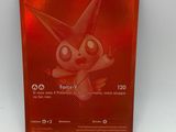 La carte Pokémon est posée sur une surface blanche avec un fond rouge.