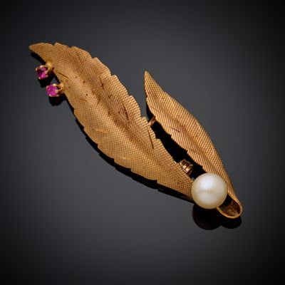 un gros plan d'une broche ornée d'une perle et d'une feuille d'or