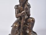 bronze statue of a man sitting on a rock with a rifle