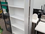 a tall white bookcase next to a chair in a warehouse