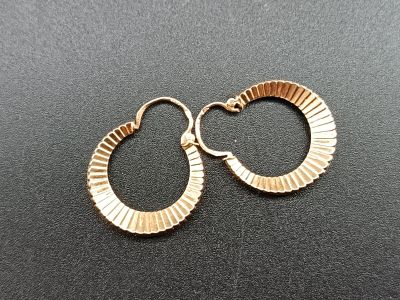 a close up of a pair of gold earrings on a black surface