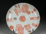 une assiette orange et blanche, ornée d'inscriptions en caractères asiatiques, posée sur un socle