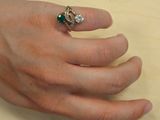 a woman ' s hand holding a ring with a green and white stone