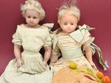 two dolls sitting next to each other on a pink surface