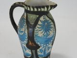 a blue and white vase with a black handle on a white surface