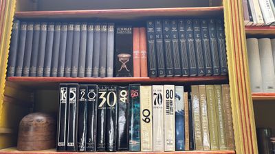 une bibliothèque sur laquelle sont rangés de nombreux livres, avec une horloge posée dessus