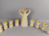 des vases et des tasses rayés de jaune et de blanc, disposés en cercle sur une surface grise