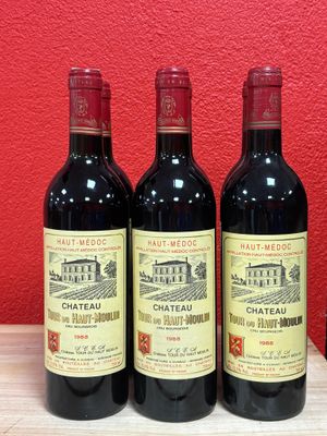 three bottles of red wine sit on a table in front of a red wall