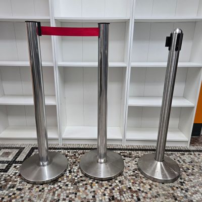 three stainless steel poles with red ribbon on them in front of a bookcase