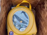 un petit sac à dos jaune dans un panier posé par terre