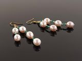 a pair of pearl and emerald earrings on a black surface