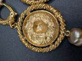 a close up of a necklace with a gold coin and a pearl