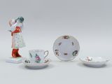 three porcelain figurines of a woman and two cups and saucers