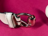 a white leather belt with a silver buckle on a pink surface