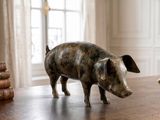 une statue représentant un cochon debout sur une table, à côté d'un stylo et d'un encrier