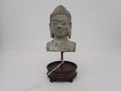 statue représentant une tête de Bouddha posée sur un socle en bois, sur une surface blanche