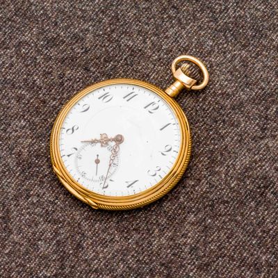 une montre de poche en or avec un cadran blanc sur un fond marron