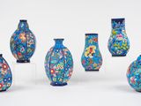 six vases bleus ornés de motifs floraux sont alignés sur une surface blanche