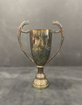 Coupe-trophée ancienne plaquée argent, posée sur un socle, sur fond gris