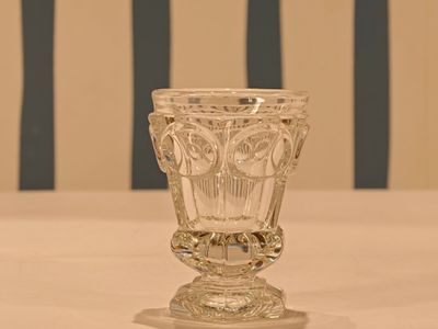 a glass vase sitting on a table with a striped chair in the background