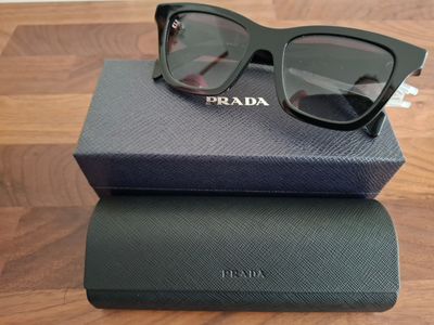 Lunettes de soleil Prada dans leur boîte et leur étui, posées sur une table en bois