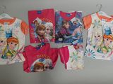 plusieurs t-shirts pour enfants à l'effigie des princesses de « La Reine des neiges » accrochés à un mur