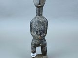 statue d'un homme coiffé d'un chapeau, assis sur un socle en bois