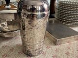 un shaker à cocktail argenté posé sur une table, à côté d'une pile d'assiettes
