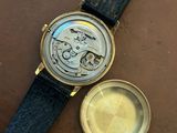 a close up of a watch with a gold case and a black leather strap