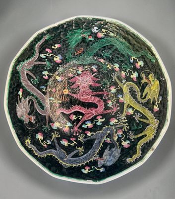 une assiette noire ornée d'un motif représentant un dragon et des fleurs