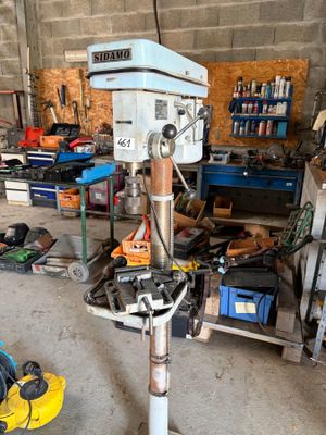 une perceuse posée sur un support dans un garage, avec des outils