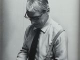 black and white photograph of a man in a shirt and tie cutting a piece of paper