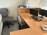a desk with two computers and a chair in the corner