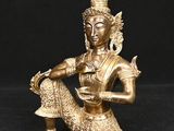 une statue en or représentant une femme assise sur un rocher, tenant un oiseau dans la main