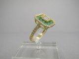 une bague sertie d'une émeraude et de diamants, posée sur un présentoir transparent