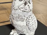 sculpture of an owl sitting on a black table in front of a fence