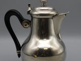 a silver coffee pot with a black handle on a gray surface